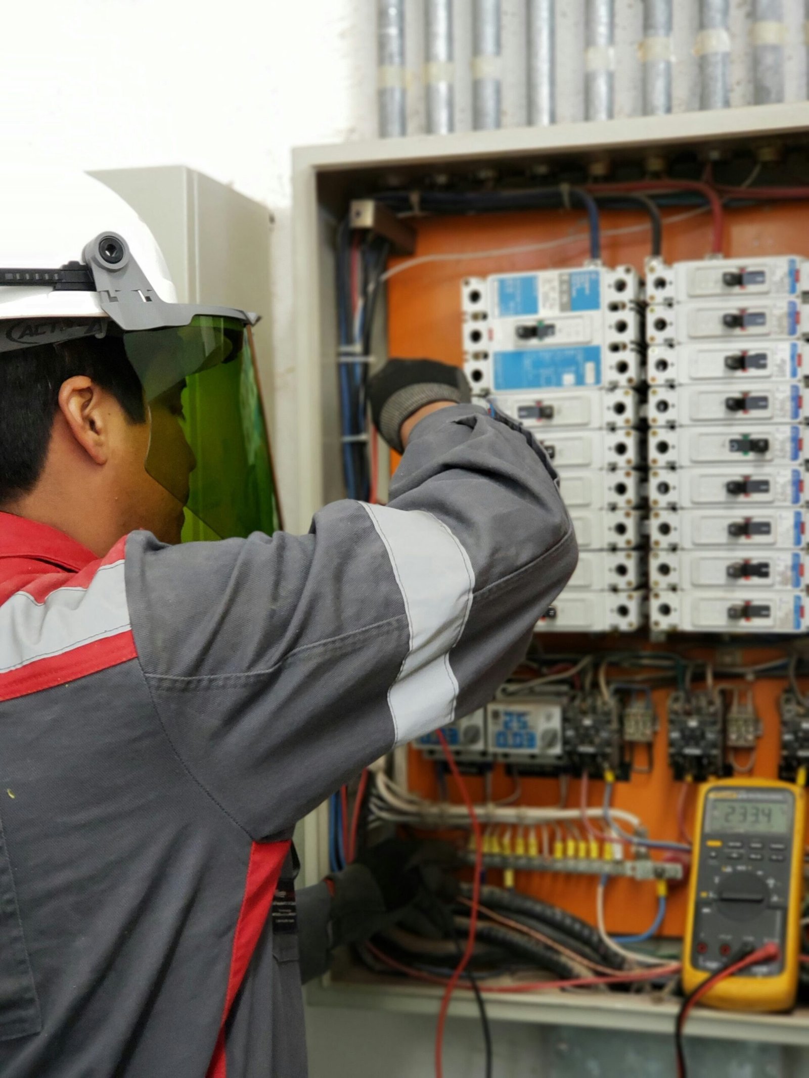 Industrial electrical technician repairing wiring and circuit breakers inside a control cabinet.